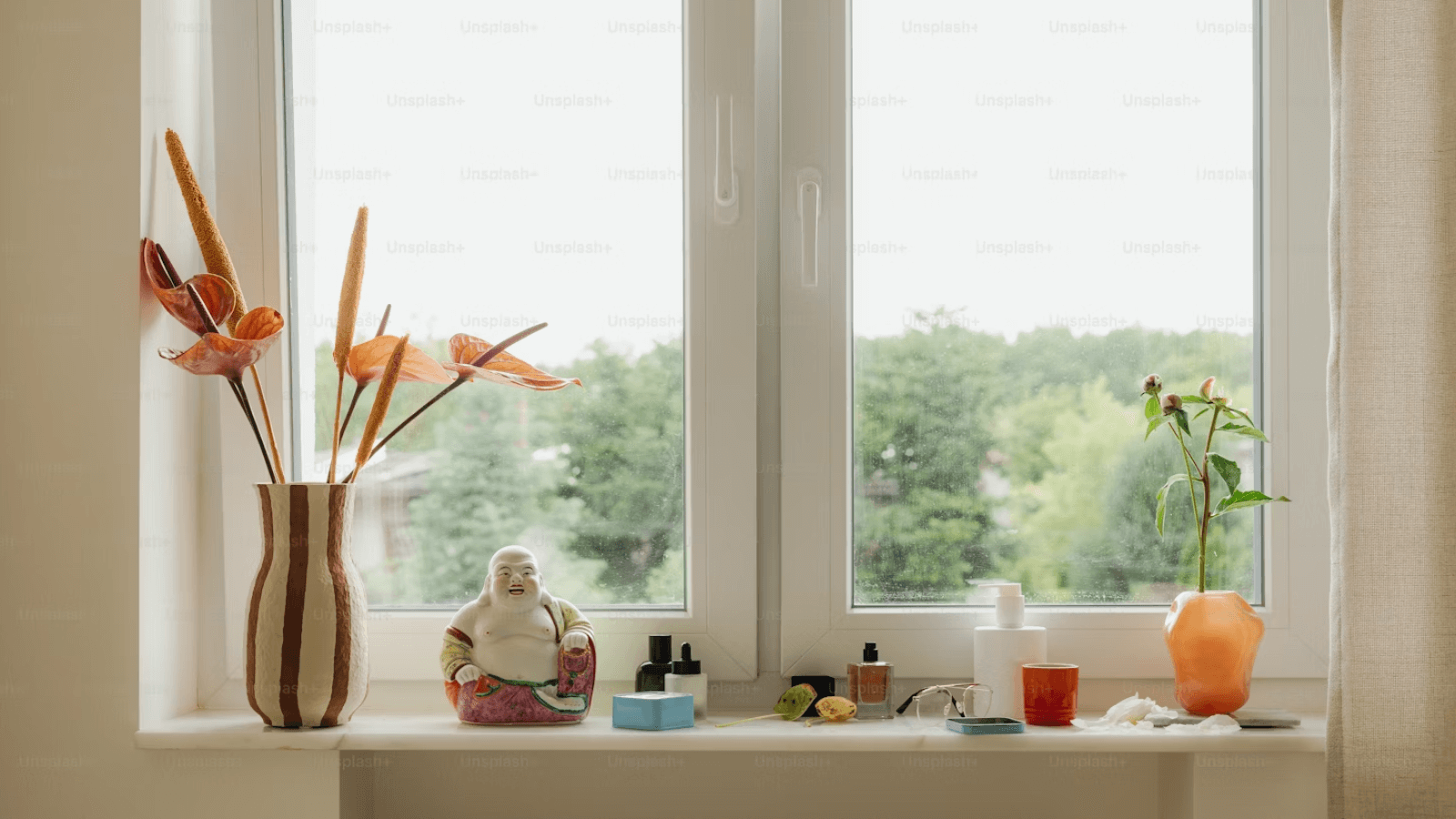 A bright windowsill featuring vases with flowers, small decorative items, and a laughing Buddha figurine.