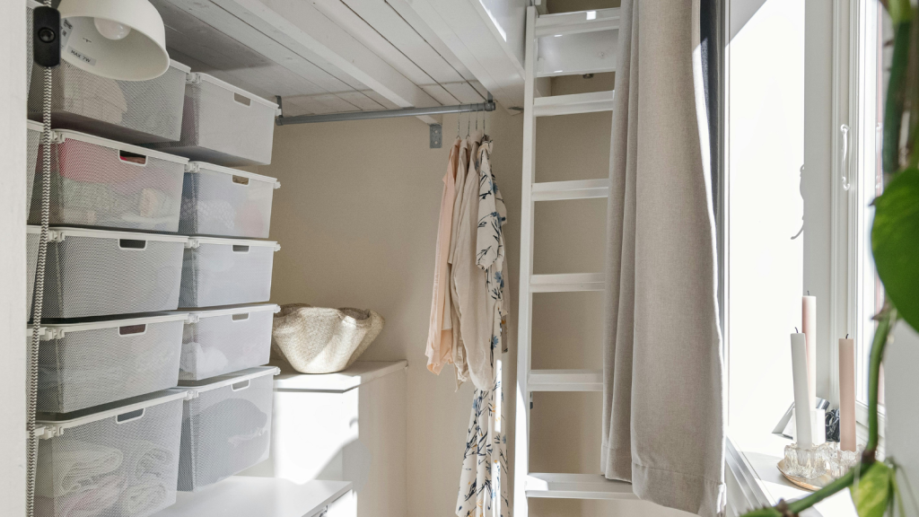 A bright, compact closet with stacked mesh drawers, a few hanging clothes, and sunlight streaming through the window.