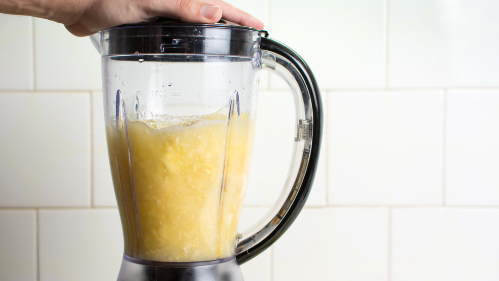 A blender filled with chopped yellow fruit being blended on a kitchen counter.