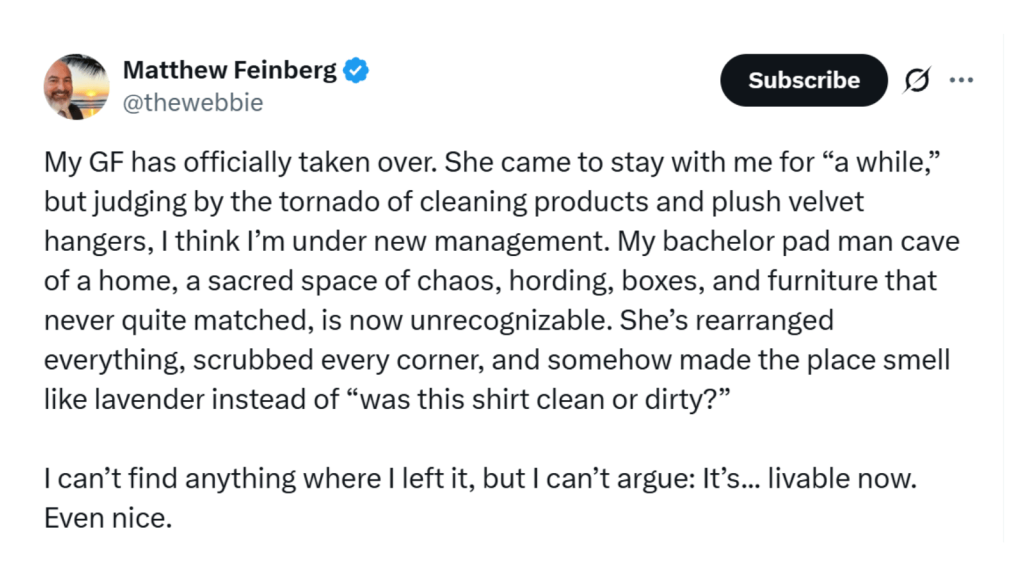 Screenshot of an X post from “Matthew Feinberg” (@thewebbie). In a long humorous paragraph he says his girlfriend came to stay “for a while” and now he’s under new management: his chaotic bachelor-pad man cave full of boxes and mismatched furniture has been completely rearranged, scrubbed, and made to smell like lavender. He can’t find anything anymore, but admits the place is now livable—even nice.