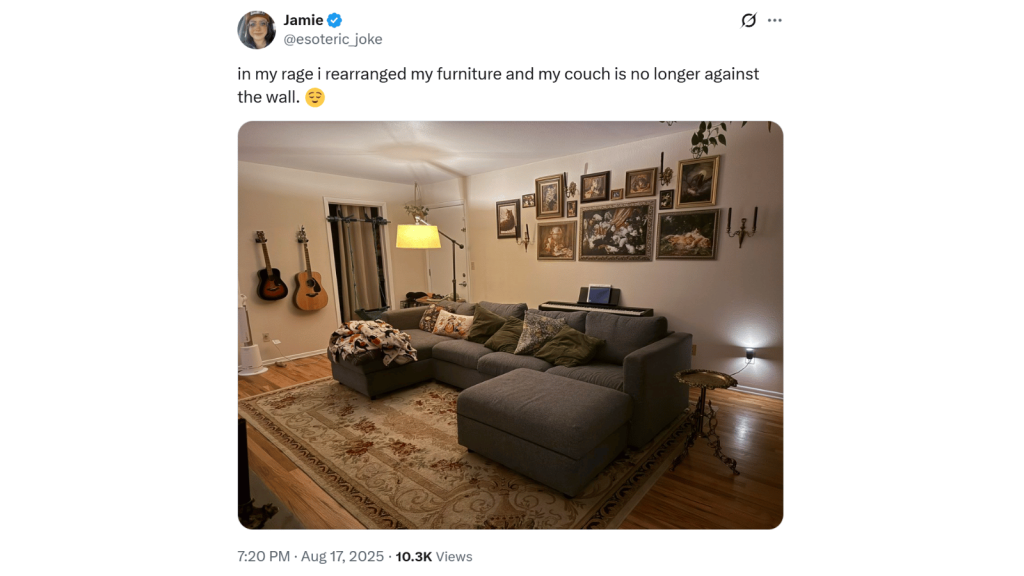 Screenshot of an X post from Jamie (@esoteric_joke). The post reads, “in my rage i rearranged my furniture and my couch is no longer against the wall.” A warm-lit living room photo shows a gray sectional now positioned away from the walls, surrounded by guitars, framed art, and soft lighting.
