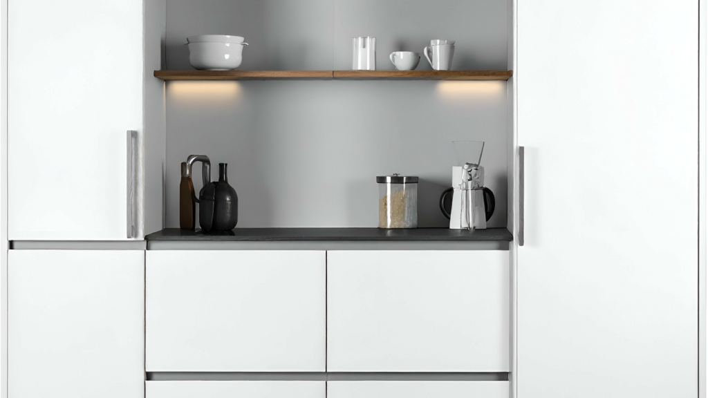 A modern white kitchen with sleek cabinets, wooden open shelving, and simple dishes and bottles neatly arranged.