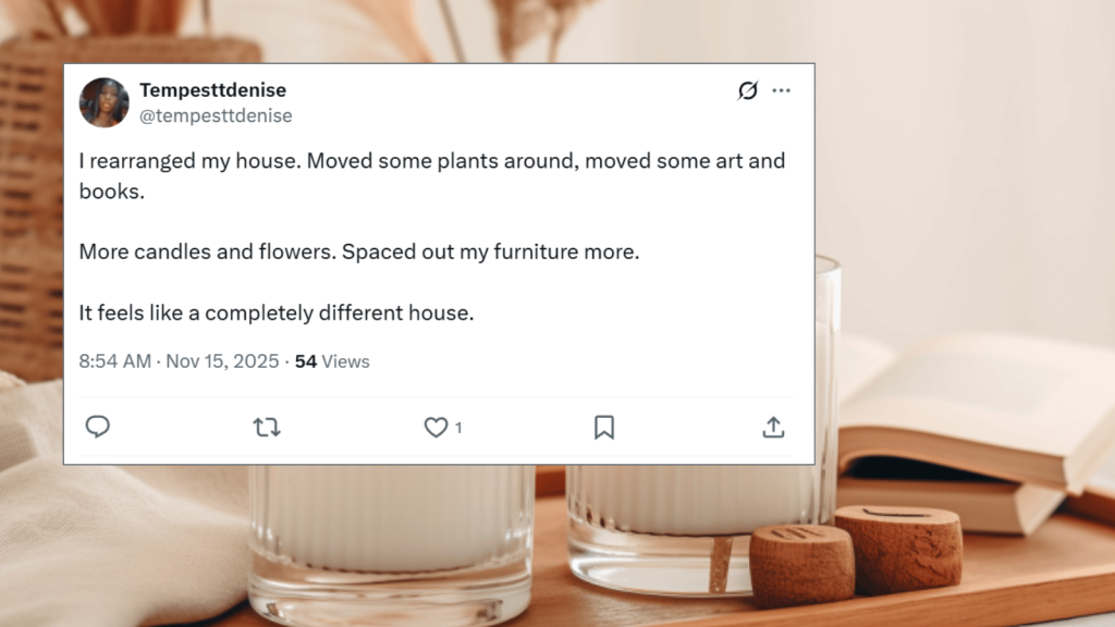 Screenshot of an X post from Tempesttdenise (@tempesttdenise). The post says they rearranged their house by moving plants, art, and books, adding more candles and flowers, and spacing out furniture. They write that the home now feels completely different. The tweet is overlaid on a soft, aesthetic background featuring two white candles in glass jars, wooden lids, and an open book on a wooden tray.