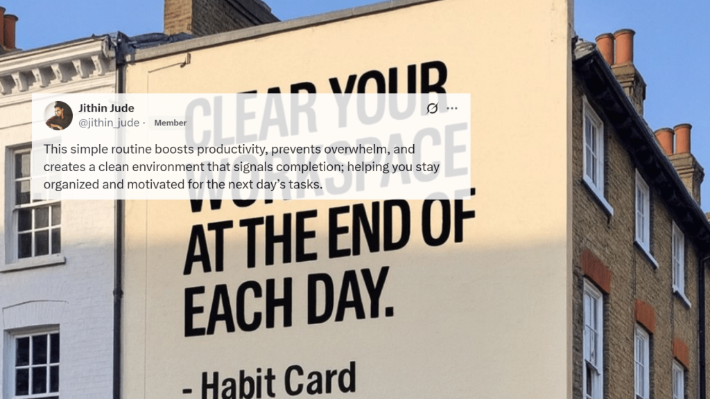 A tweet overlay appears on a photo of a large beige building with bold black text painted on the side reading “CLEAR YOUR WORKSPACE AT THE END OF EACH DAY. – Habit Card.” Nearby buildings frame the scene.