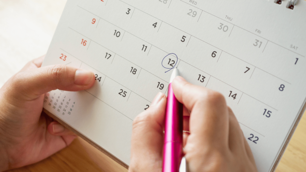 A close-up of a hand holding a pen and circling a date on a paper calendar, symbolizing planning or designating specific times of the year for organizing or resetting a space.