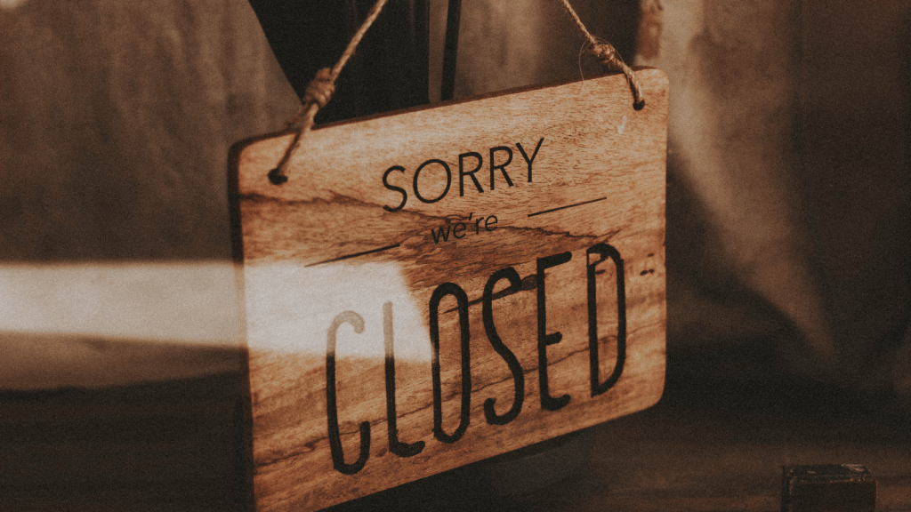A wooden sign hanging by a cord reads “SORRY we’re CLOSED.” The lighting is warm and soft, emphasizing the texture of the wood.