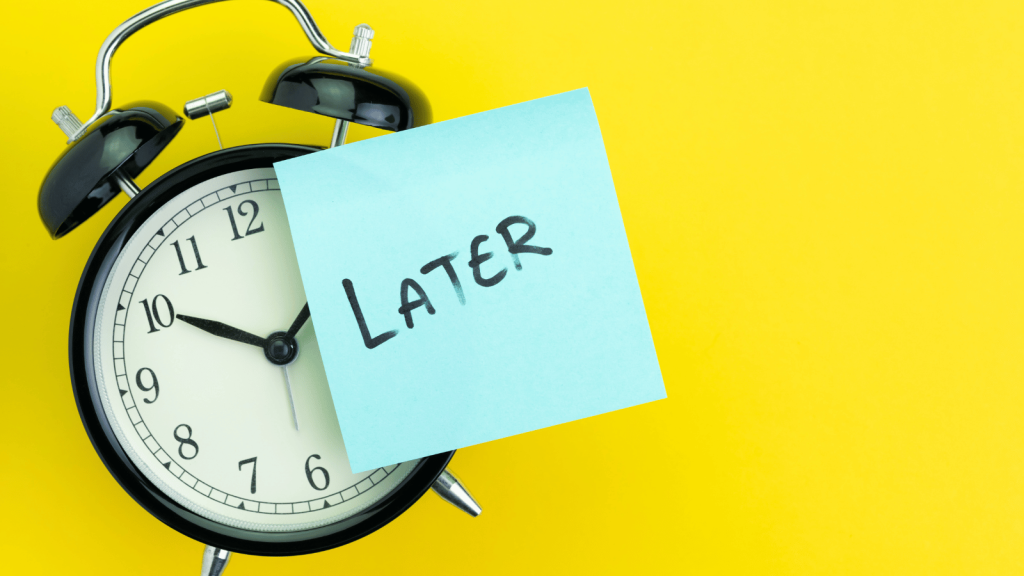 A black retro-style alarm clock sits against a bright yellow background with a blue sticky note covering part of its face. The note reads “LATER” in bold black handwriting.