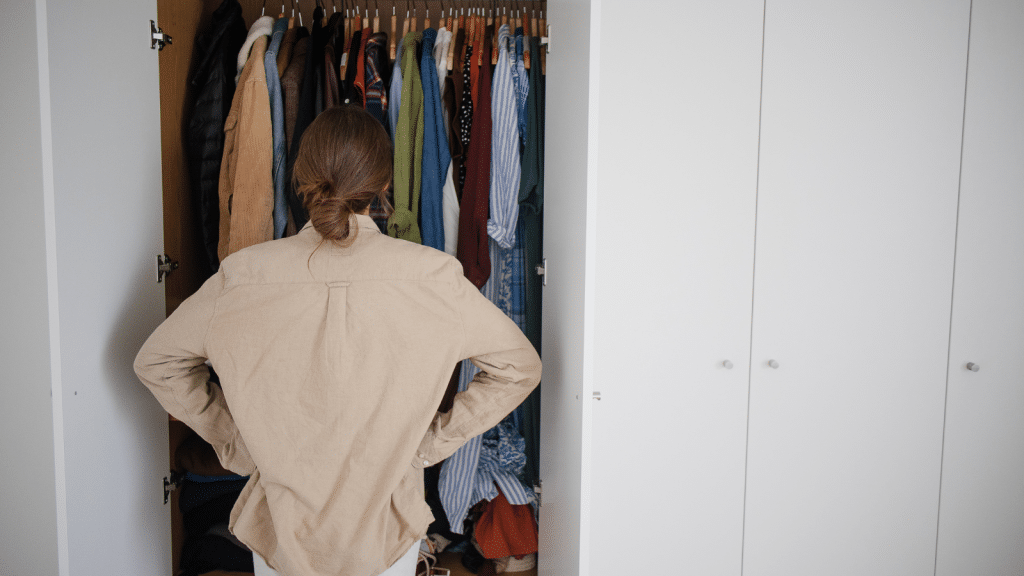 Person standing in front of a crowded closet, illustrating simple closet fixes that start with editing and decluttering clothes.
