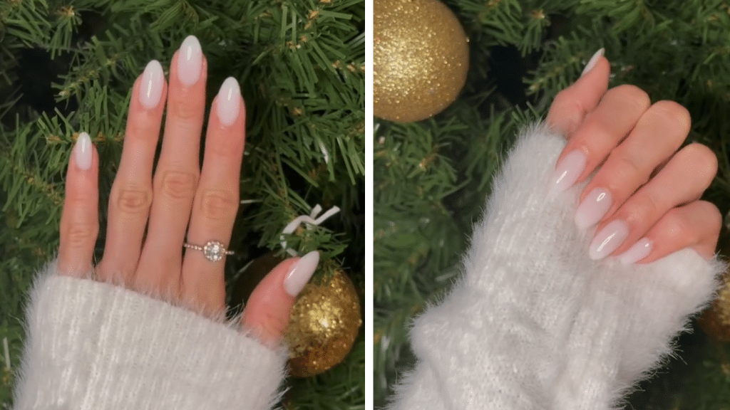 Almond-shaped creamy white ombré nails with a glossy finish, photographed against a Christmas tree with gold ornaments. A fuzzy white sweater and a diamond ring enhance the soft, elegant look, giving the manicure an old money Christmas nails feel. These Christmas nails feature a clean, luxurious neutral style.