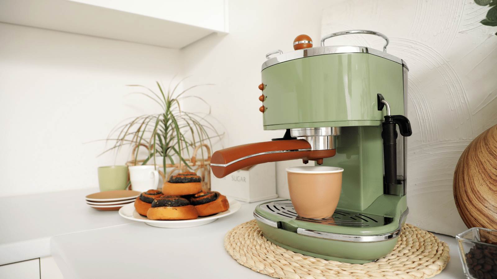 best-coffee-makers-countertop-display Retro green espresso machine on a styled kitchen counter with a woven placemat, matching mug, and pastries